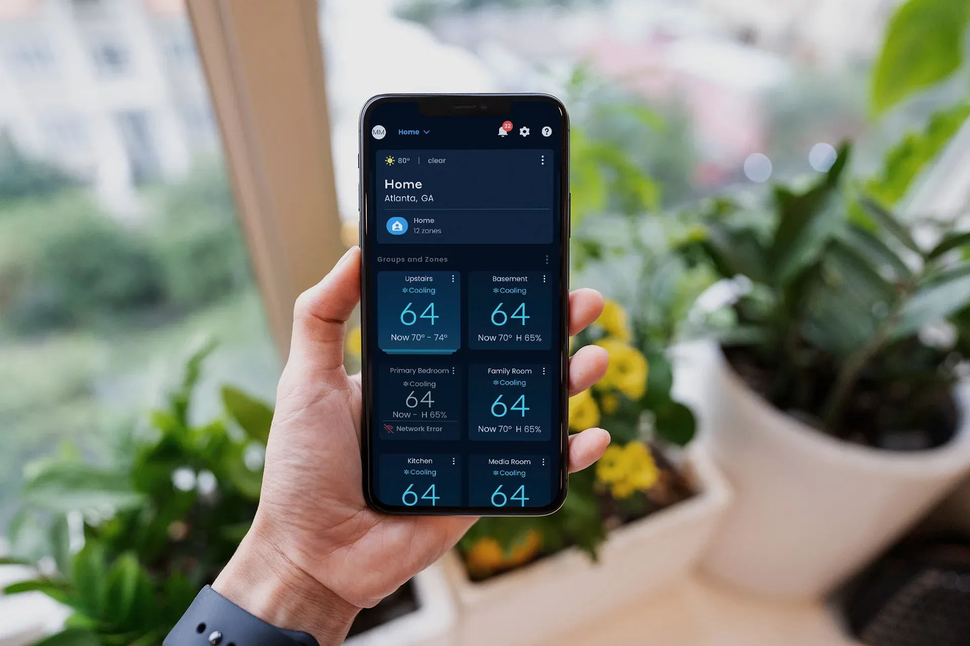 hand holding smartphone with mitsubishi comfort app on screen showing temperatures in multiple rooms