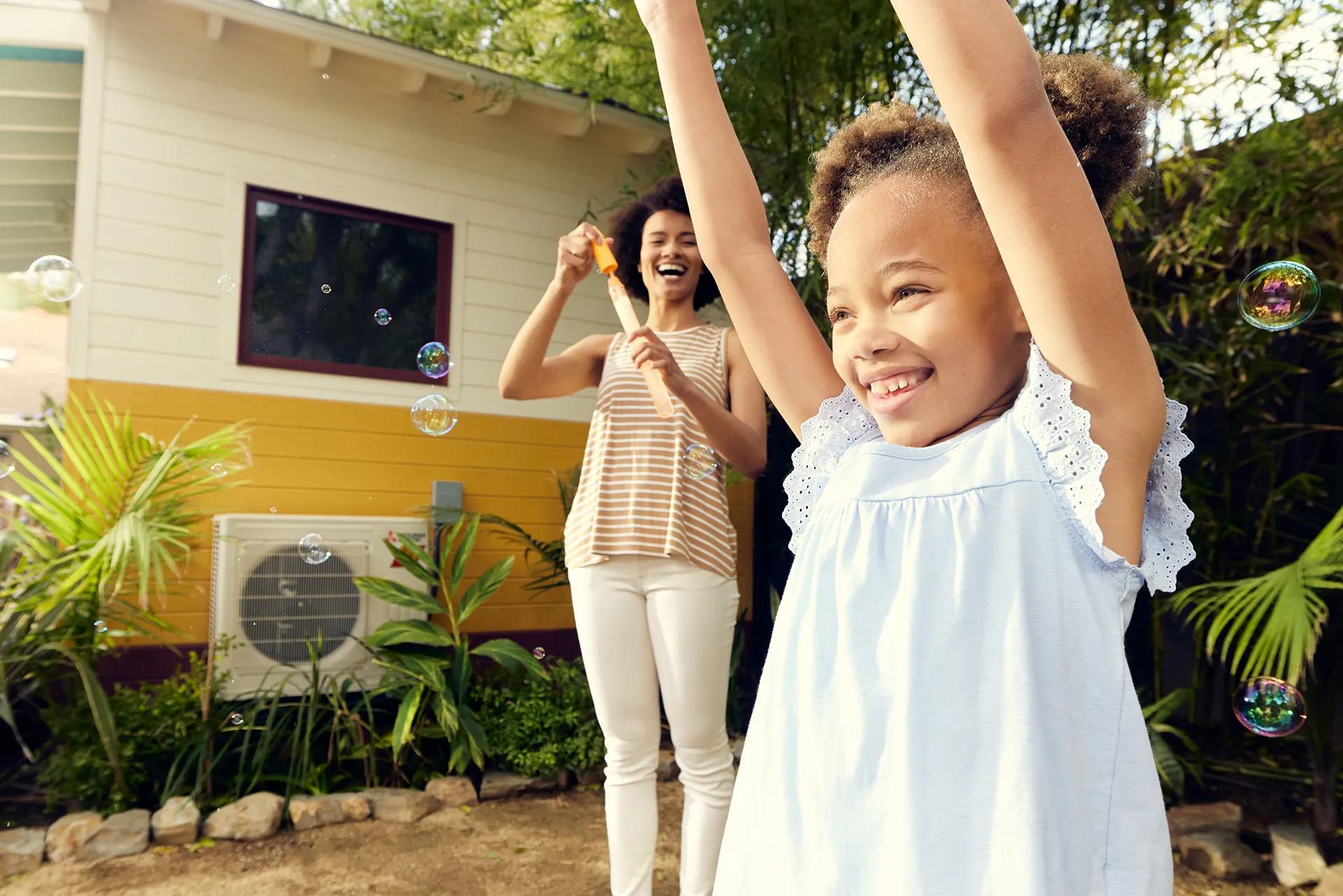 Mother and young daughter playing with bubbles by outdoor heat pump