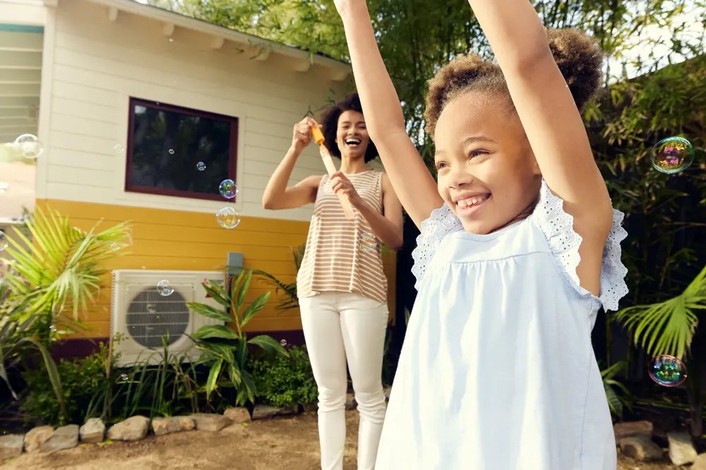 Mother and young daughter playing with bubbles by outdoor heat pump